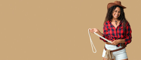 Beautiful African-American cowgirl with lasso on beige background