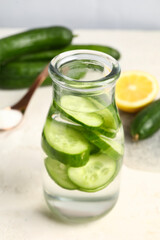 Bottle of infused water with cucumber slices on white table