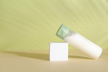 Bottle of cosmetic product, plaster podium and palm leaf shadow on green background