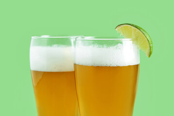 Glasses of cold beer with lime on green background