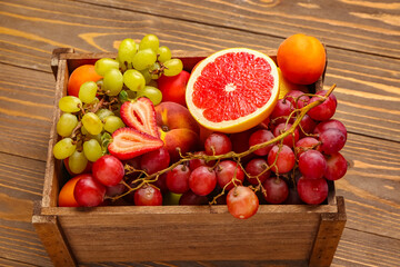 Box with different fresh fruits on wooden background