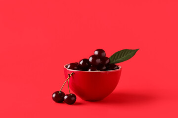 Bowl with sweet cherries and leaf on red background