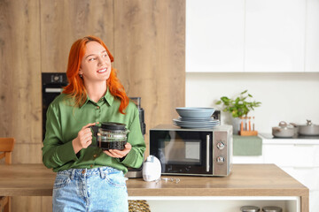 Young redhead woman with coffee pot in modern kitchen
