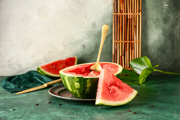 Plate with half of fresh watermelon and pieces on green table