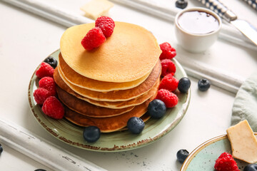 Plate of tasty pancakes with raspberries and blueberries on white wooden background