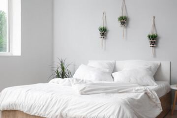 Interior of light bedroom with large double bed, white pillows and houseplants