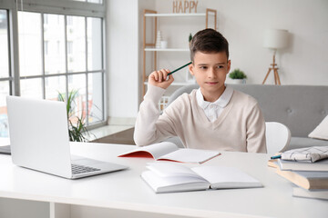 Thoughtful little boy studying online with laptop at home