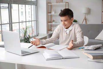 Confused little boy studying online with laptop at home