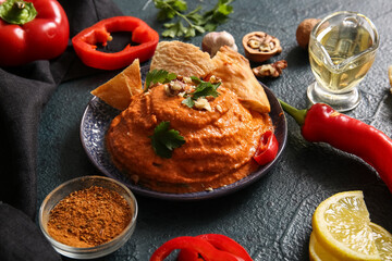 Plate of tasty muhammara and ingredients on black background