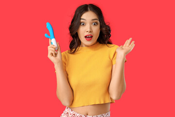Beautiful young shocked Asian woman with vibrator on red background