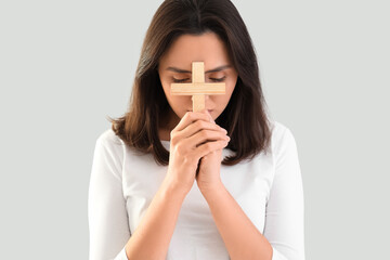 Young woman praying with cross on light background, closeup