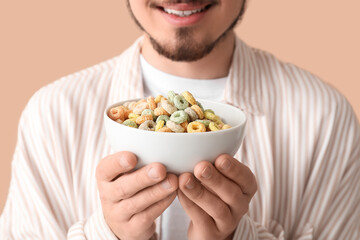 Man holding bowl with cereal rings on beige background, closeup