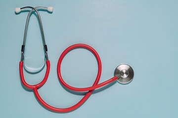 Vibrant red stethoscope, earpieces top, diaphragm right, on light blue. Ideal for healthcare, medical care, diagnosis, and general health awareness.
