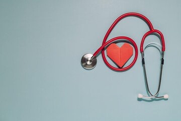 Red stethoscope with its diaphragm by a red origami heart on light blue. Perfect for themes of heart health and compassionate medical care.