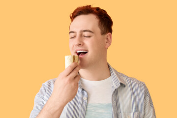 Young man eating tasty doner kebab on beige background