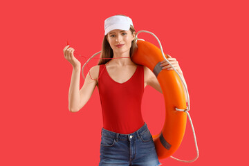 Young female lifeguard in cap with whistle and rescue ring on red background