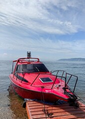 Obraz premium vibrant red speedboat is moored at wooden dock along calm waters. clear blue sky and distant hills create picturesque setting, perfect for day exploring. close up.