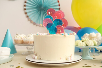 Table with cake, sweets and decor for birthday party against white wall