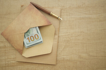 Money in an envelope with a pen on a wooden desk