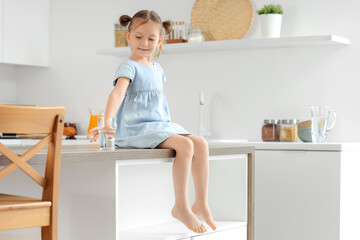 Cute little girl with glass of water sitting on table in kitchen