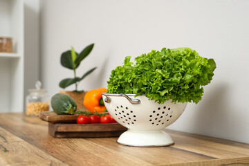 Colander with fresh lettuce on wooden kitchen counter