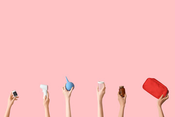 Hands with enema, first aid kit, pills and thermometer on pink background