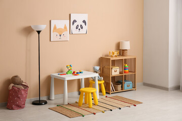 Interior of children's room with play table, lamps and many toys in shelving unit near beige wall