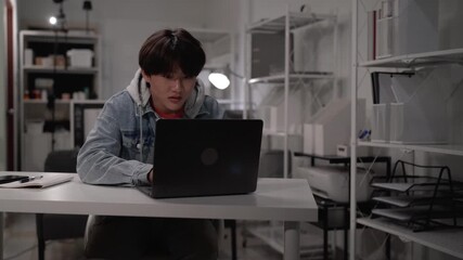 Asian young adult student programmer intently working laptop computer at modern home office desk focused on coding problem solving technology solutions learning education - Powered by Adobe