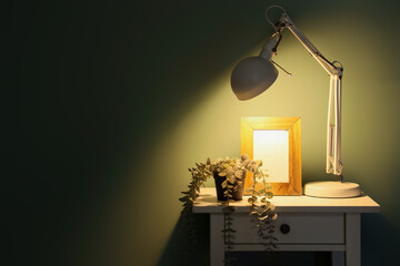 Glowing lamp with frame and plant on table in dark room