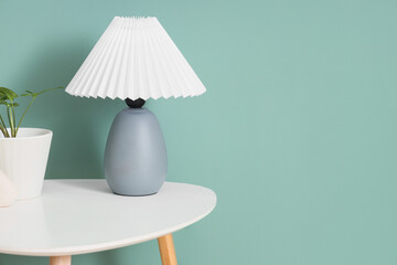 Stylish lamp with plant on table near green wall