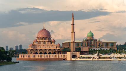 Obraz premium Putra Mosque and Perdana Putra, by Putrajaya Lake, Putrajaya, Malaysia. Iconic pink mosque and government office building under a cloudy sunset sky