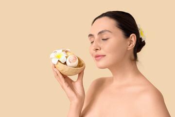 Young woman with bath bombs and plumeria flowers on beige background, closeup