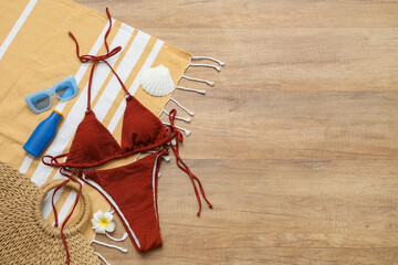 Stylish swimsuit, bottle of sunscreen cream and beach accessories on wooden floor, closeup
