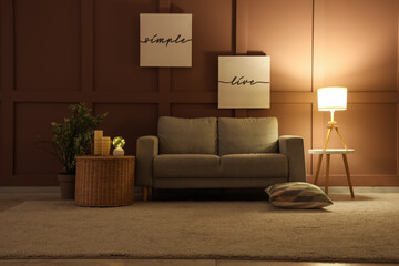 Interior of living room with glowing lamps, sofa and basket in evening