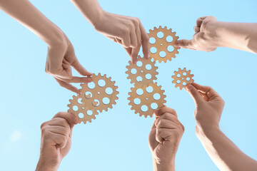Many hands with wooden gears against sky, bottom view