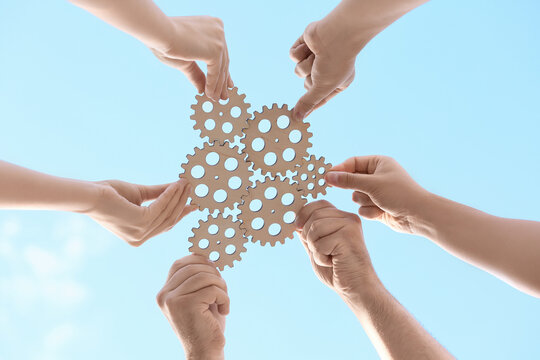 Many hands with wooden gears against sky, bottom view - Powered by Adobe