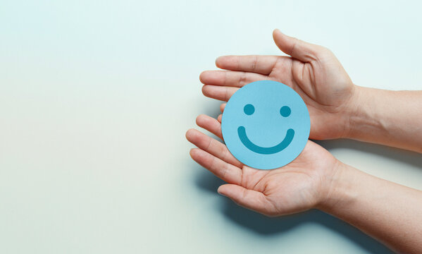 paper cut smiley face in hands on light blue background. positive thinking, mental health, assessment, world mental health day concept