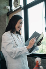 A female doctor in a white coat reviews patient records in a well-lit medical office, exuding...