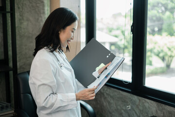 Female doctor in white coat reviewing documents in a bright, modern medical office setting.