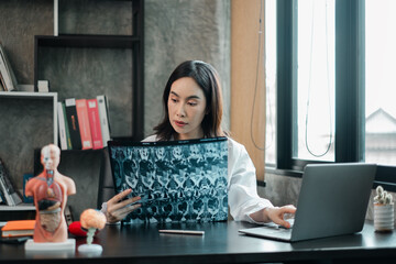 Female doctor examines X-ray in a contemporary office setting, surrounded by anatomical models and...