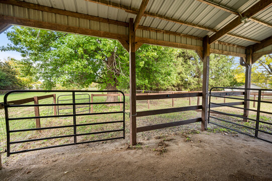 Functional outdoor horse stall with a covered roof and open sides, providing shelter and ventilation in a rural farm setting.
