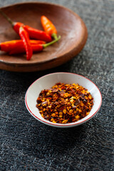 Red chili flakes, red pepper flakes, in a white porcelain sauce cup, placed on grey fabric napkin....
