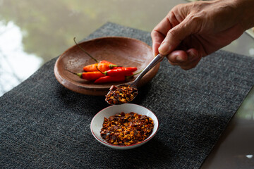 people hand holding chili flakes, red pepper flakes, using a tablespoon. Shot over grey fabric napkin. In cozy home environment