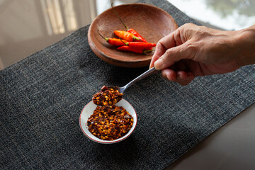 people hand holding chili flakes, red pepper flakes, using a tablespoon. Shot over grey fabric napkin. In cozy home environment