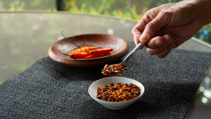 people hand holding chili flakes, red pepper flakes, using a tablespoon. Shot over grey fabric napkin. In cozy home environment
