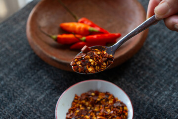 people hand holding chili flakes, red pepper flakes, using a tablespoon. Shot over grey fabric napkin. In cozy home environment