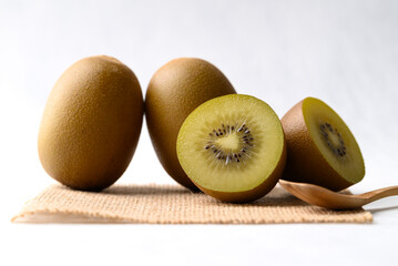 Fresh sungold kiwi fruit on burlap fabric and wooden spoon on white background, Healthy eating