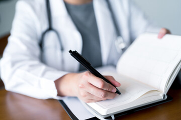 Doctor writing on an open planner notebook for scheduling appointments or recording patient notes, wearing a stethoscope and lab coat, symbolizing medical planning and healthcare documentation tasks.
