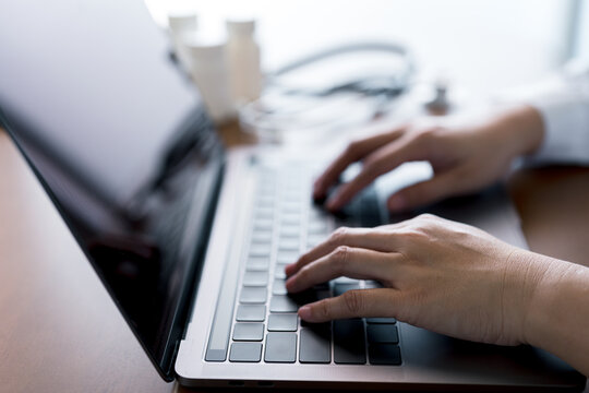 Close-up hands of doctor typing on laptop keyboard with stethoscope and medicine bottles, representing digital healthcare, online consultation, telemedicine services and medical data management.