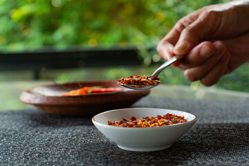people hand holding chili flakes, red pepper flakes, using a tablespoon. Shot over grey fabric napkin. In cozy home environment